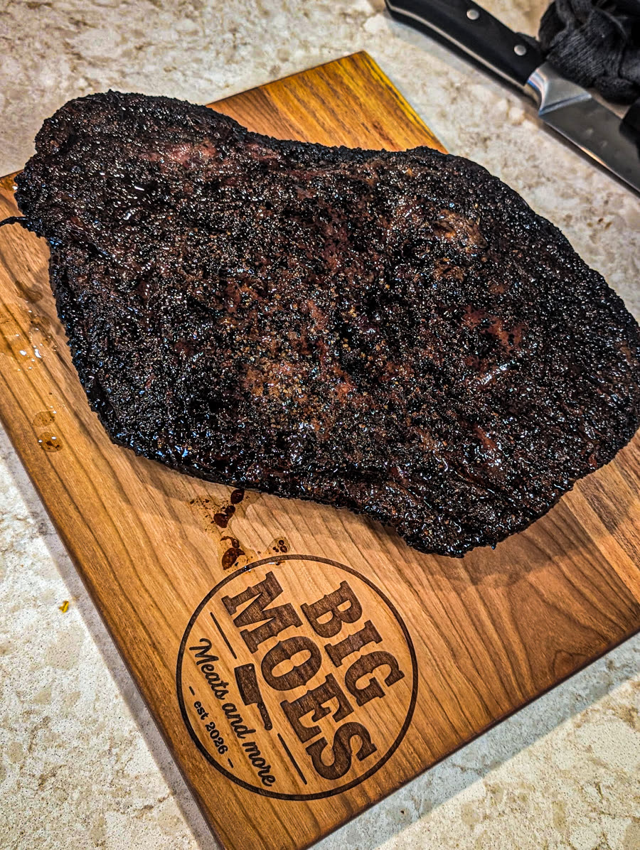 Whole smoked brisket with a dark peppery bark resting on a Big Moe's branded cutting board