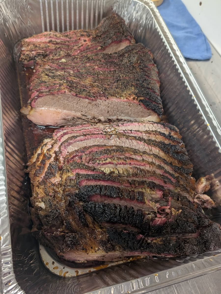Sliced smoked brisket with a peppery bark and deep pink smoke ring, piled in a catering tray