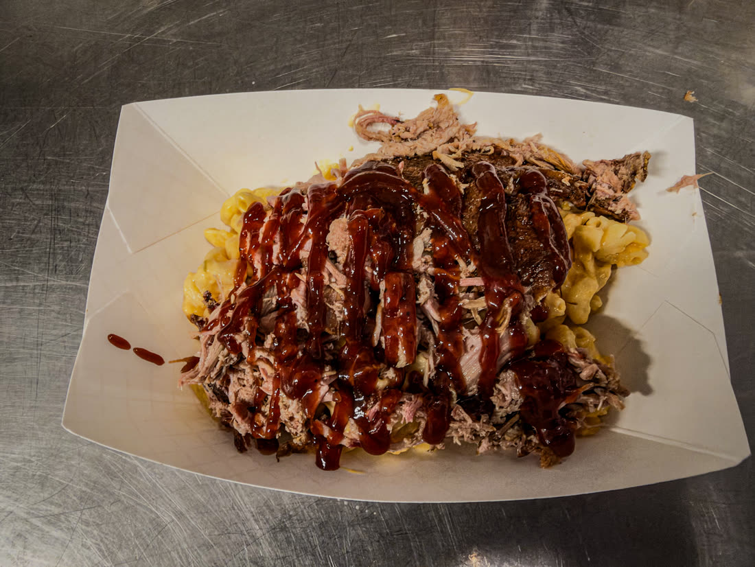 Loaded mac and cheese topped with pulled pork and barbecue sauce in a paper boat