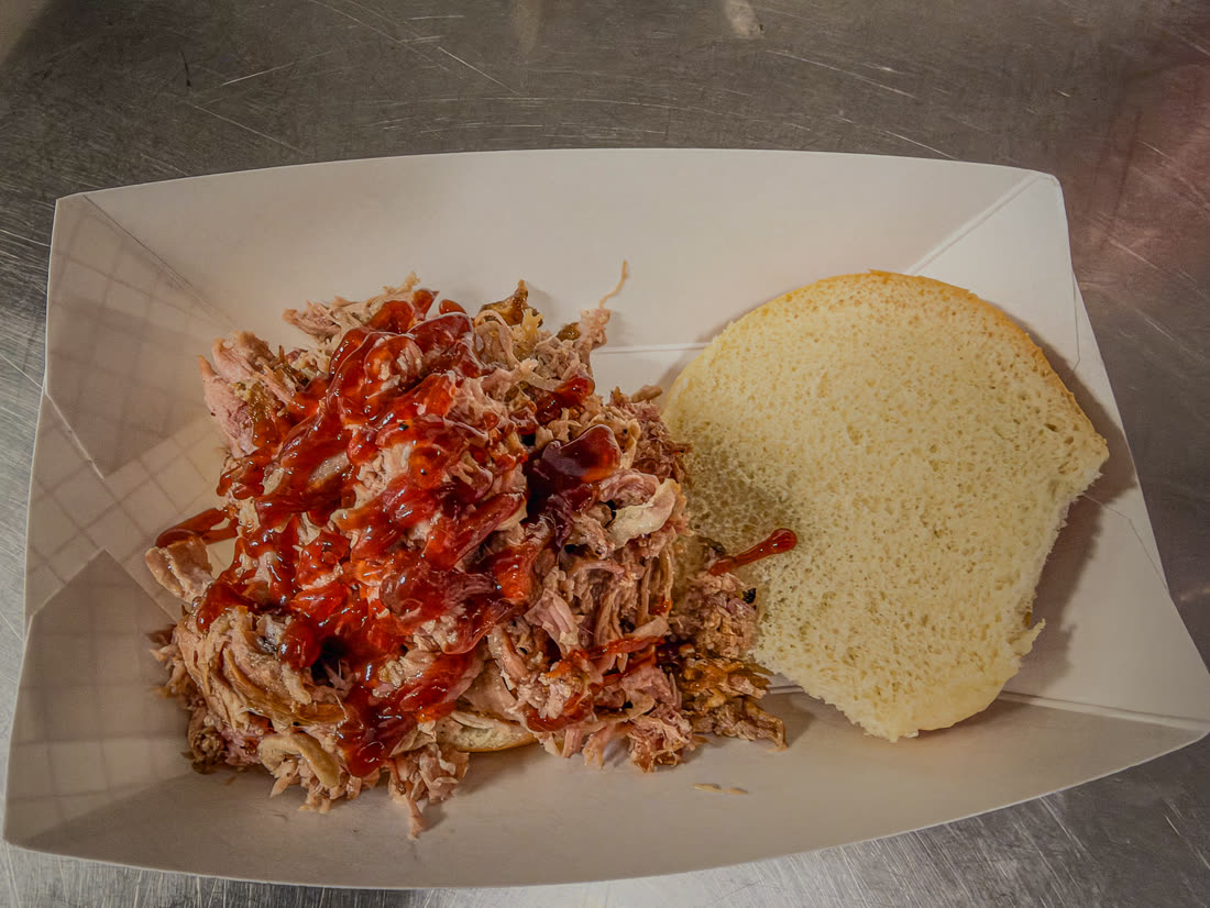 Pulled pork drizzled with barbecue sauce next to a soft bun in a paper boat