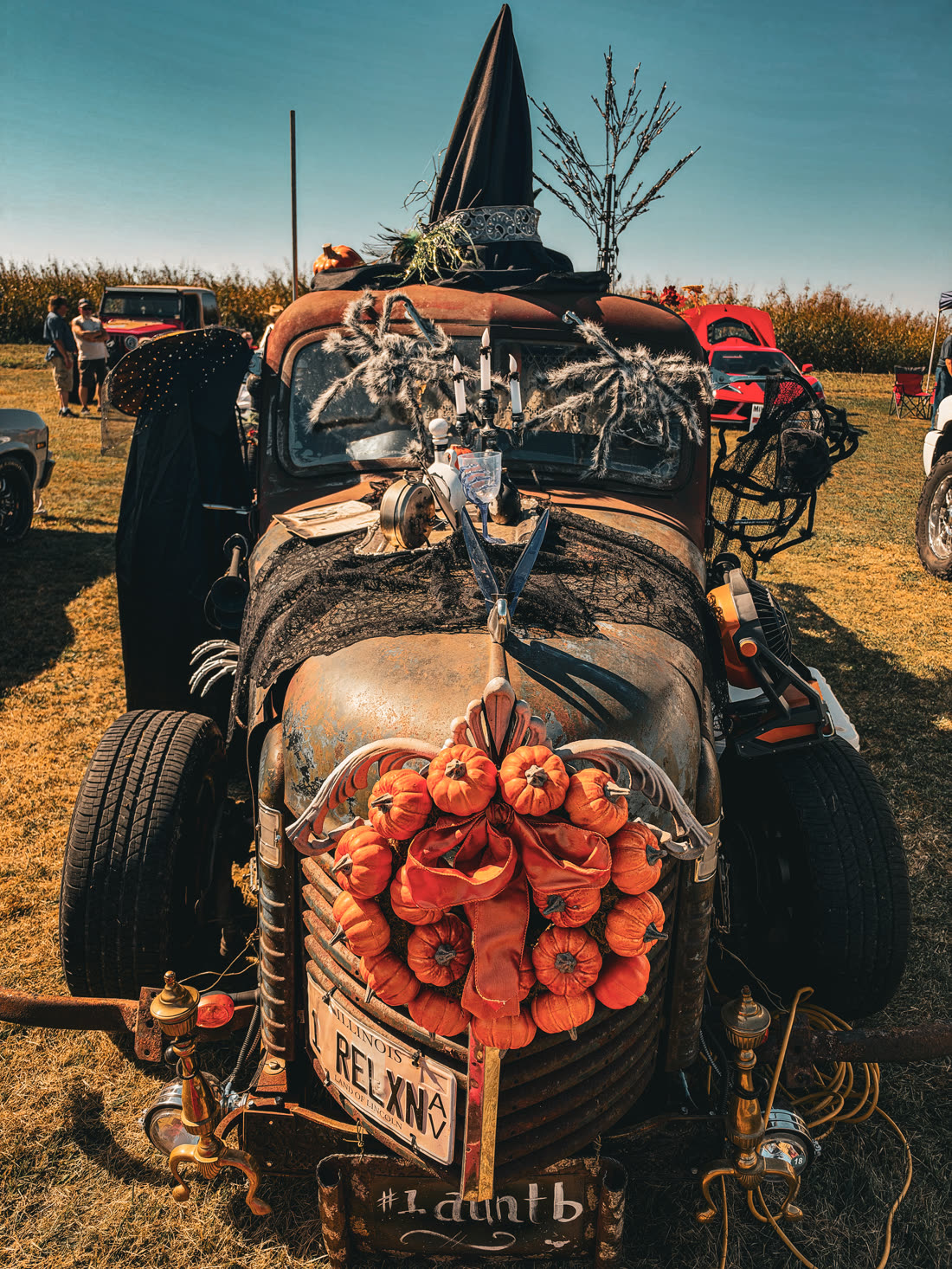 Halloween-decorated rat rod truck with a witch hat and a grille full of mini pumpkins at the car show
