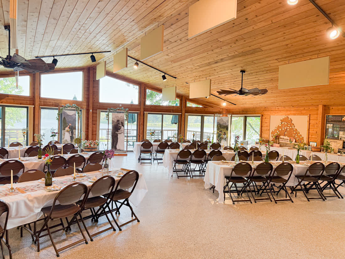 Wedding reception hall set up with long tables, white linens, and a rustic wood-beam ceiling